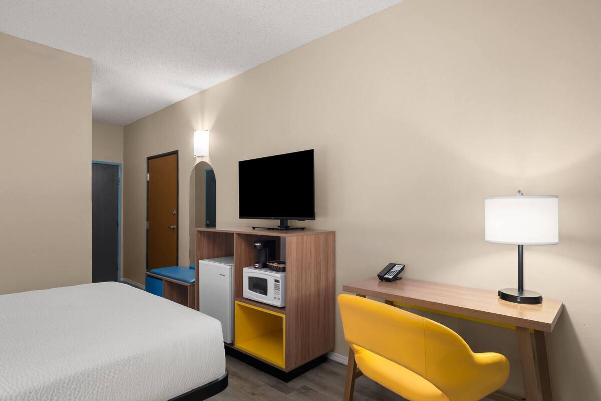 A hotel room with a bed, a desk with a lamp, a television, a microwave, and a small refrigerator.