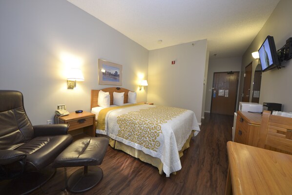 A hotel room with a bed, a desk, a chair, a TV, and a bathroom door. - Days Inn & Suites by Wyndham Airport Albuquerque (Albuquerque)