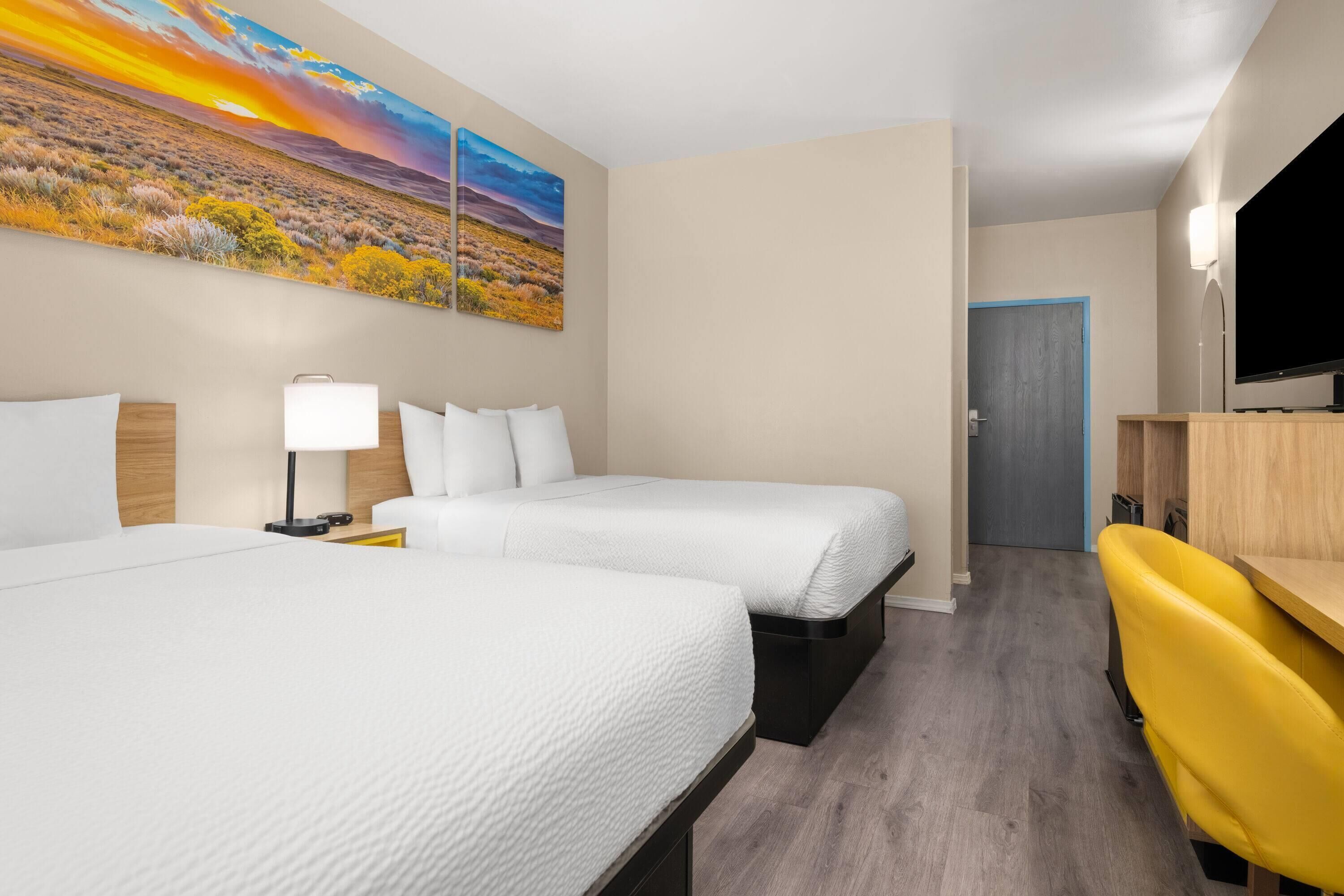 Una habitación de hotel con dos camas, un escritorio, una silla, un televisor y una puerta.