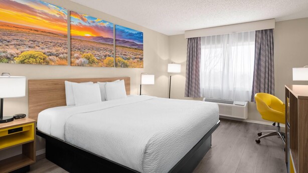 A hotel room with a large bed, a desk, a chair, and two wall-mounted lamps. - Days Inn & Suites by Wyndham Airport Albuquerque (Albuquerque)