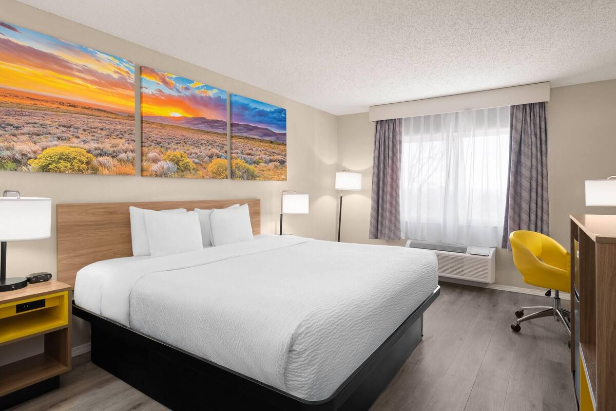 A hotel room with a large bed, a desk, a chair, and two wall-mounted lamps.