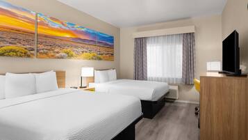Une chambre d’hôtel avec deux lits, une télévision, un bureau, une lampe et un tableau représentant un paysage au coucher du soleil.