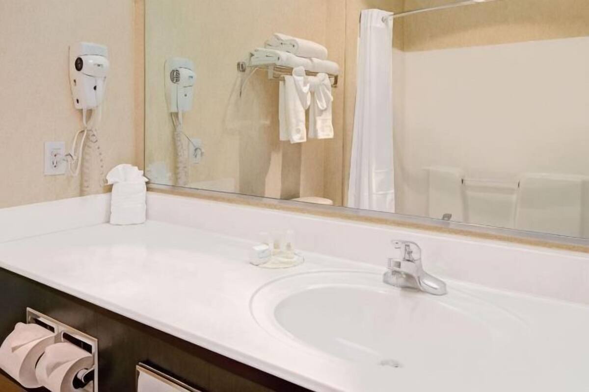 A hotel bathroom with a large sink, a mirror, a towel rack, and a hairdryer.