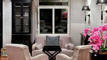 A living room with a sofa, two armchairs, a black coffee table, a cabinet, and a potted orchid plant.