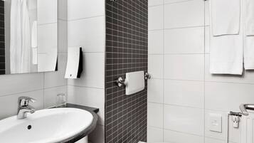 A modern bathroom with a white sink, a mirror, a towel rack, and a shower area.