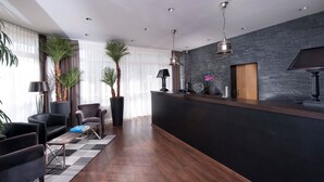 A modern reception area with a dark reception desk, black leather chairs, a wooden coffee table, and large potted plants.