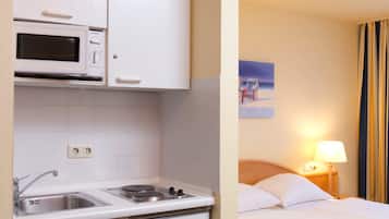 Une chambre d’hôtel avec une kitchenette équipée d’un four à micro-ondes, d’une cuisinière et d’un évier. La chambre comprend un lit, une table de chevet et une lampe.