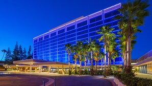 A modern hotel with a large glass facade, palm trees, and a covered entrance area. - Disneyland Hotel (Anaheim)