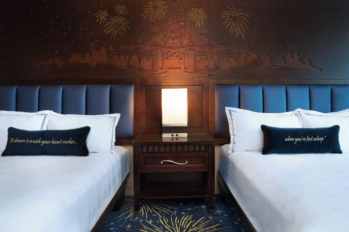 Ein Hotelzimmer mit zwei Betten, einem Nachttisch mit Lampe und einem Wandbild mit Feuerwerk.