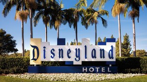 A sign for the Disneyland Hotel with a clear view of palm trees and a hedge in the background. - Disneyland Hotel (Anaheim)