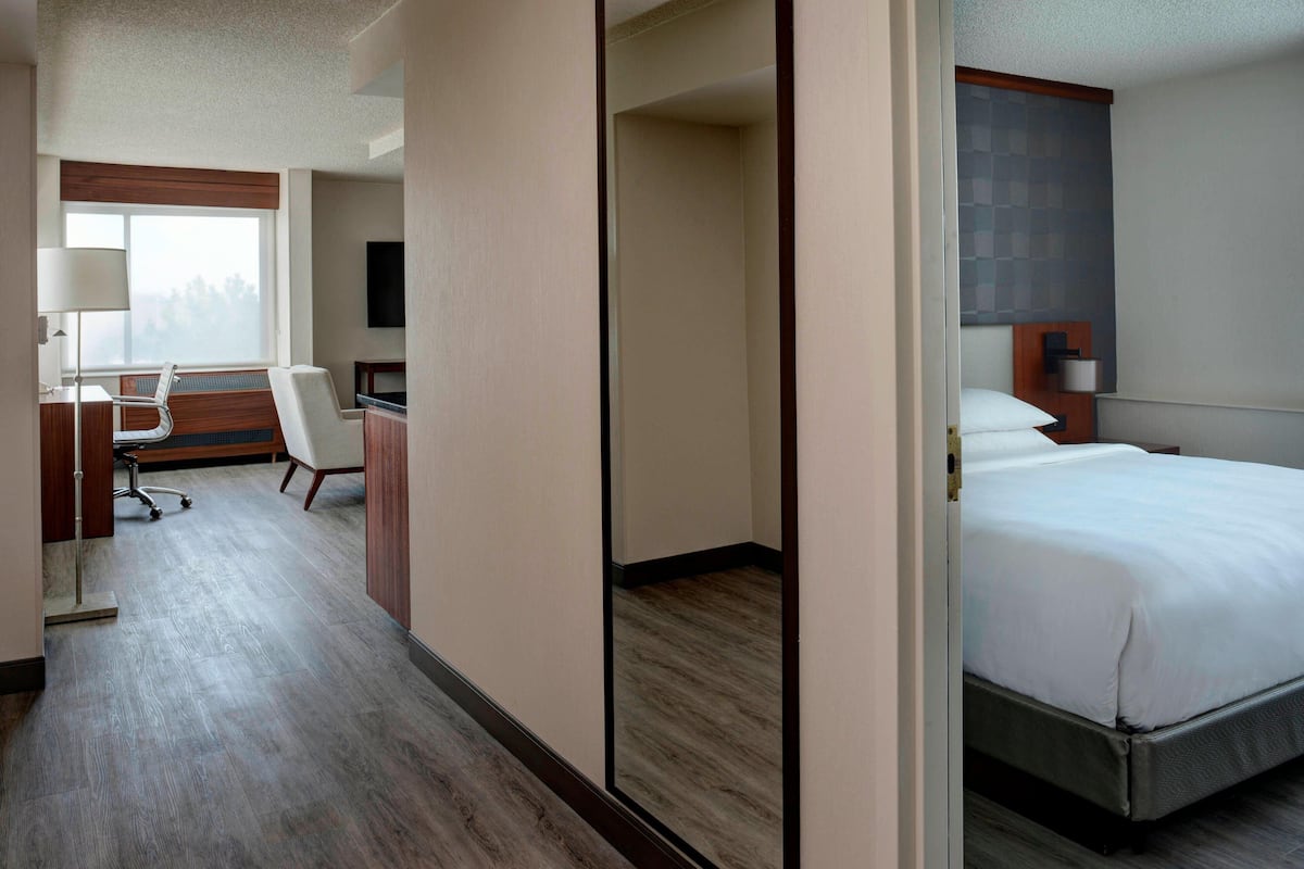 A hotel room with a bed, desk, chair, and a large window.