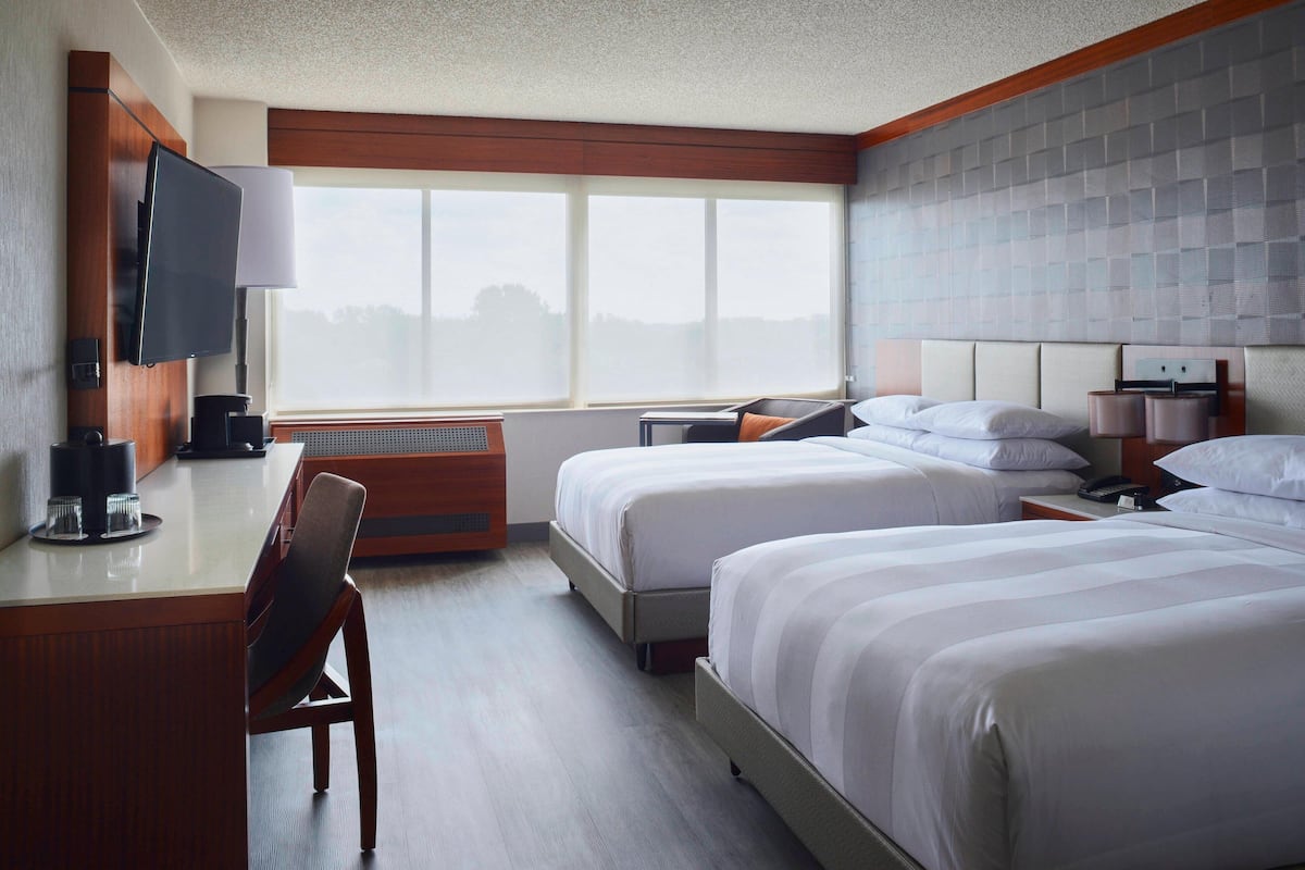A hotel room with two beds, a desk with a chair, a television, and a large window.