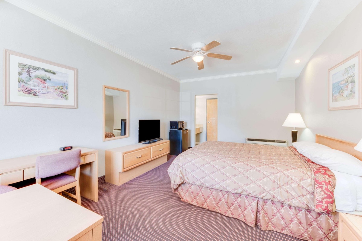 A hotel room with a bed, a desk, a television, a mirror, and a ceiling fan.
