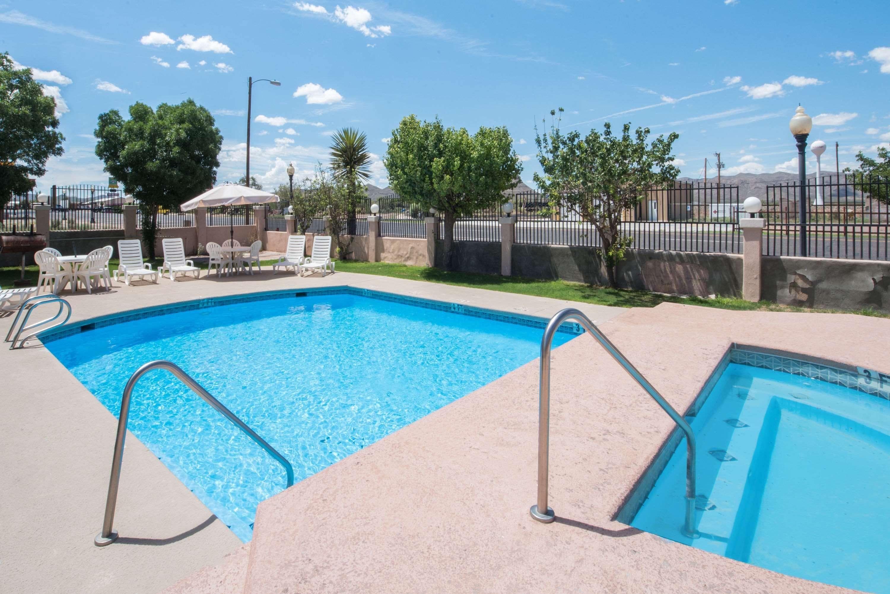Piscina retangular com escadas de metal, rodeada por espreguiçadeiras e uma cerca.