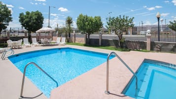 Piscina retangular com escadas de metal, rodeada por espreguiçadeiras e uma cerca.