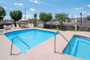 Ein rechteckiger Swimmingpool mit Metallleitern, umgeben von Liegestühlen und einem Zaun.