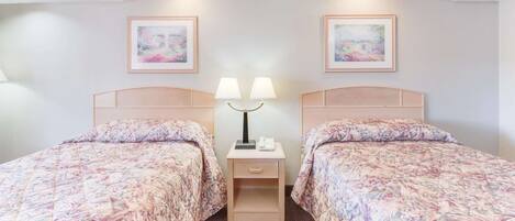 Een hotelkamer met twee bedden, elk met bloemenprint beddengoed, een nachtkastje met lampen, en twee ingelijste foto's aan de muur.