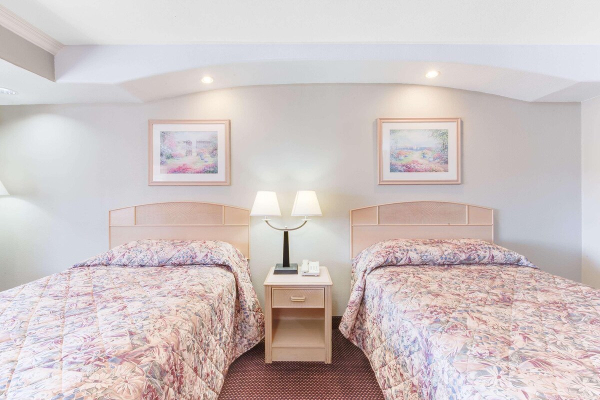 A hotel room with two beds, a nightstand with a lamp, and two framed pictures on the wall.