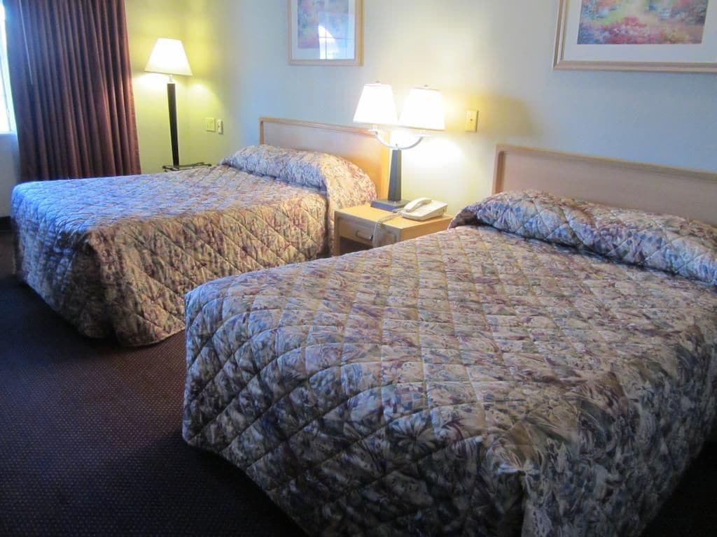 A hotel room with two beds, each with a floral-patterned bedspread, a nightstand with a lamp, and a framed picture on the wall.