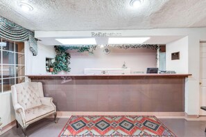 A reception area with a registration desk, a plush armchair, and a patterned rug. - Knights Inn Van Horn (Van Horn)