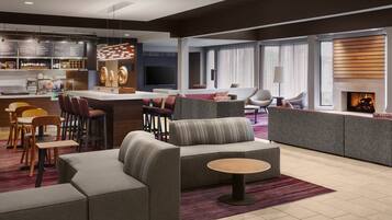 A modern hotel lobby with a bar, seating area, and a fireplace.