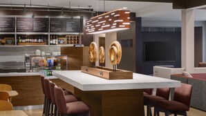A modern bar area with a wooden bar counter, a menu board, and a seating area with red chairs. - Courtyard by Marriott Mahwah (Mahwah)