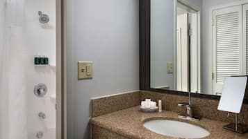 A bathroom with a granite countertop sink, a mirror, and a shower.