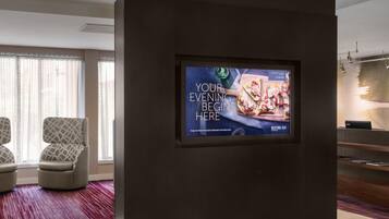 A modern hotel lobby with a large digital screen displaying a menu, comfortable seating, and a reception desk.