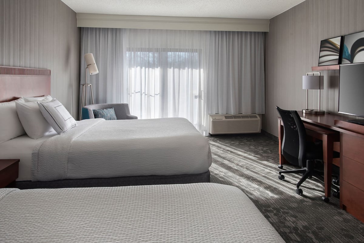 A hotel room with a large bed, a desk, a chair, and a television.