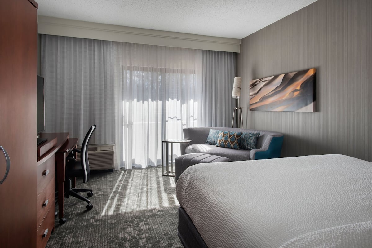A hotel room with a large bed, a desk, a chair, and a sofa.