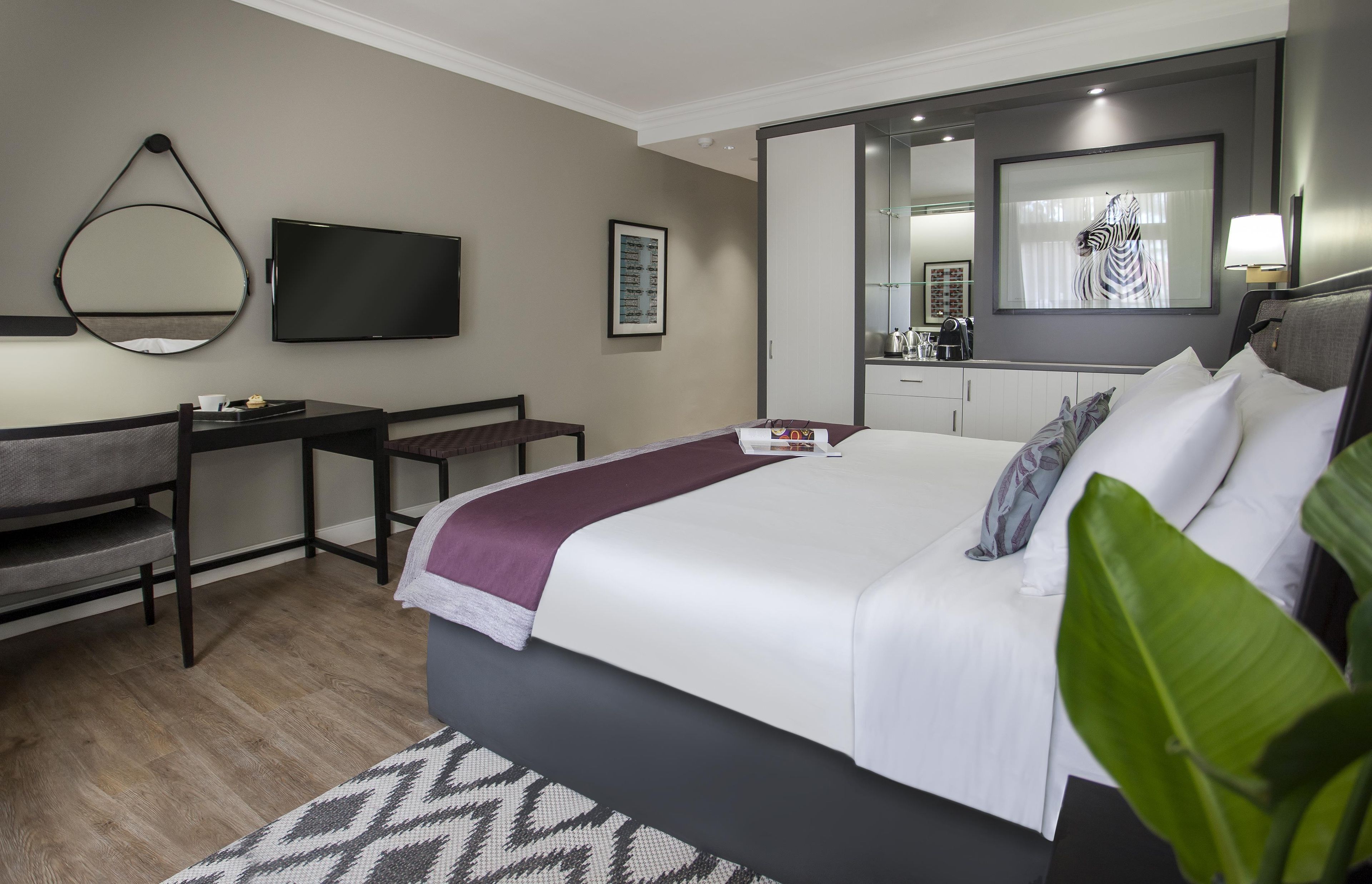 A hotel room with a bed, a desk, a chair, a television, and a mirror.