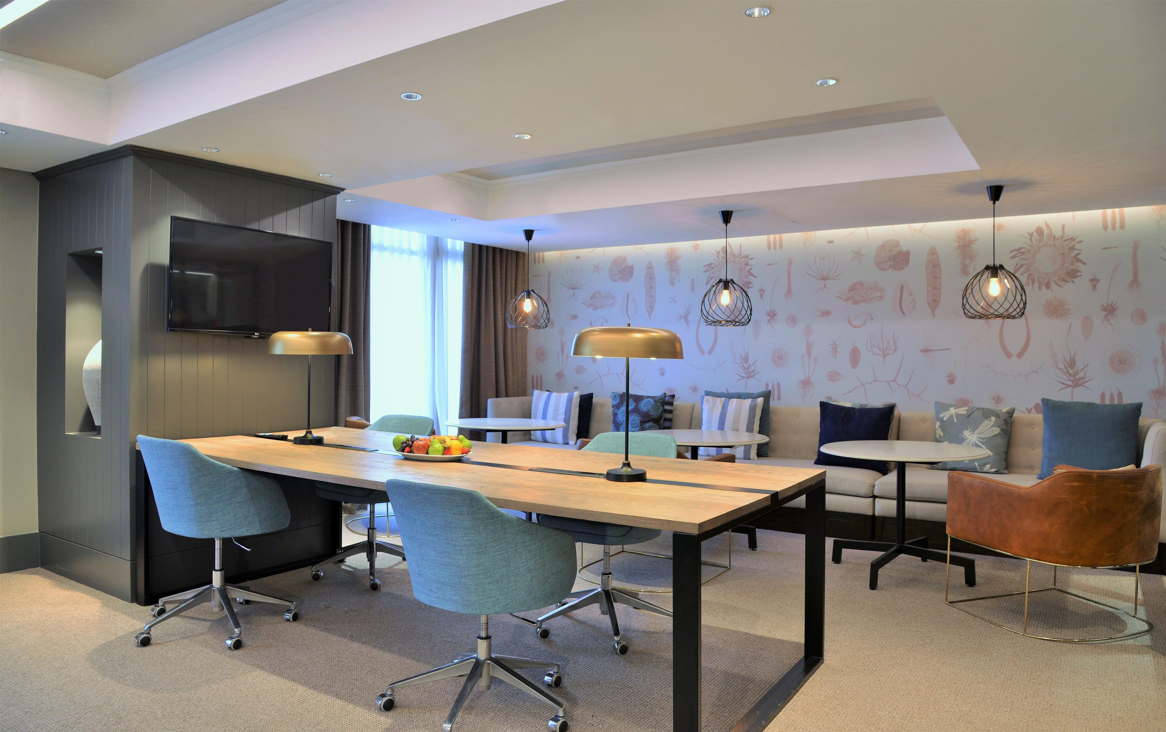 A modern hotel room with a dining area, a sofa set, and a TV mounted on the wall.