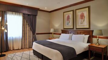A hotel room with a large bed, two bedside tables with lamps, a window with curtains, and two framed floral paintings on the wall.