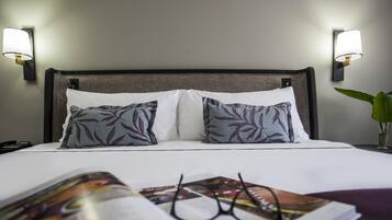 Habitación de hotel con cama, dos almohadas, mesita de noche, lámpara, teléfono y revista.