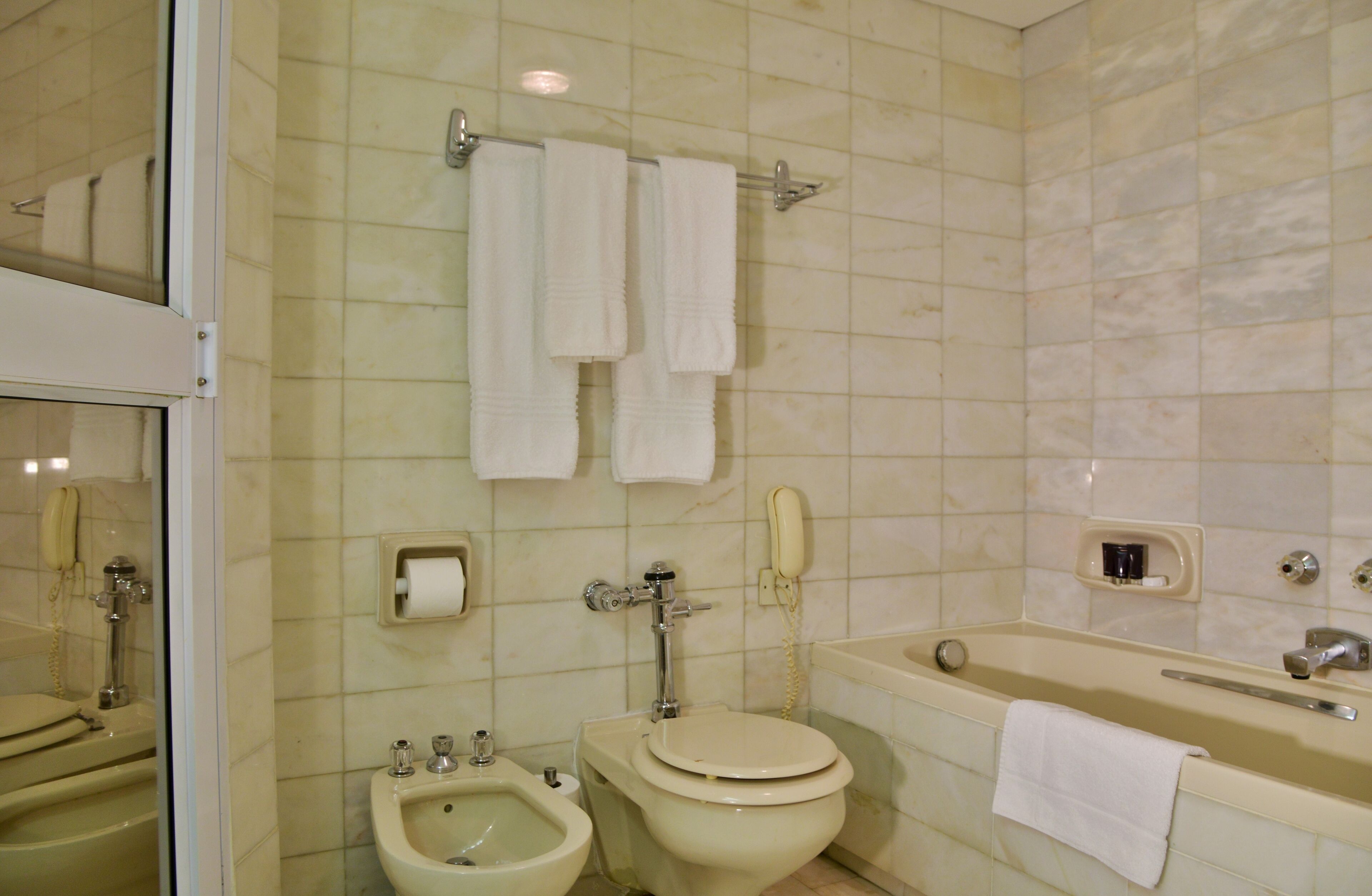A bathroom with a toilet, bidet, bathtub, and a towel rack with three towels.
