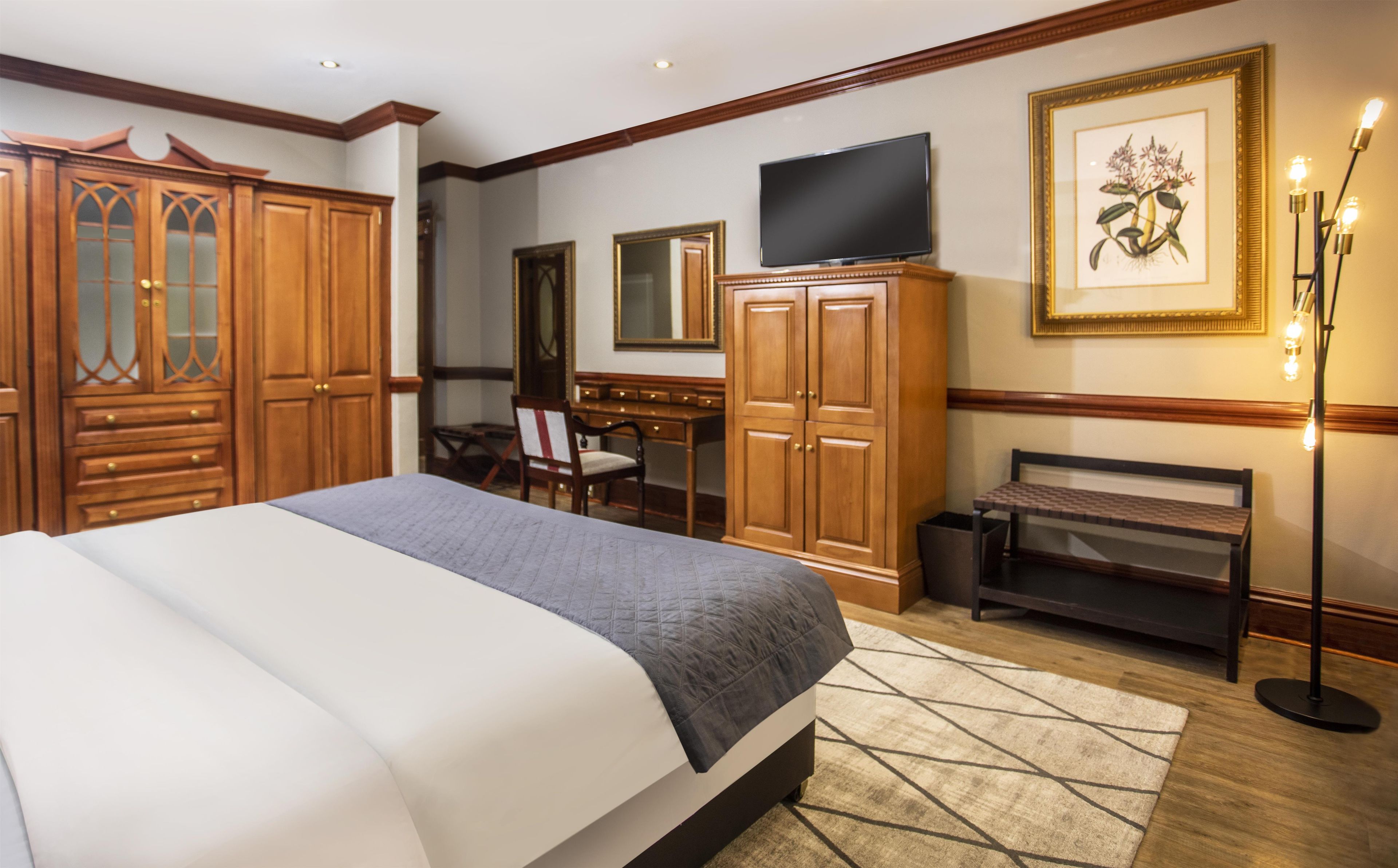 Ein Hotelzimmer mit einem großen Bett, einem Holzschrank, einem Schreibtisch mit Stuhl, einem Fernseher und einem gerahmten Bild an der Wand.