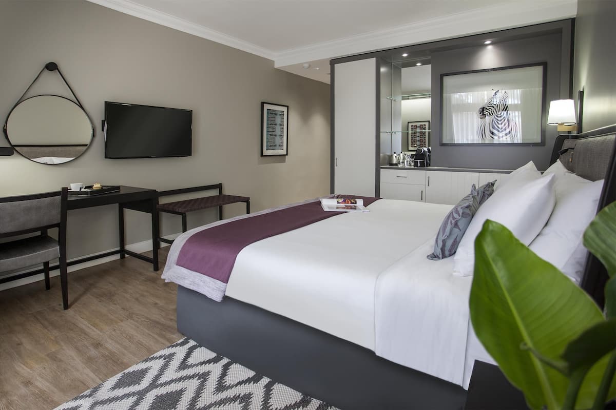 Une chambre d’hôtel équipée d’un lit, d’un bureau, d’une chaise, d’une télévision, d’un miroir et d’une grande fenêtre.