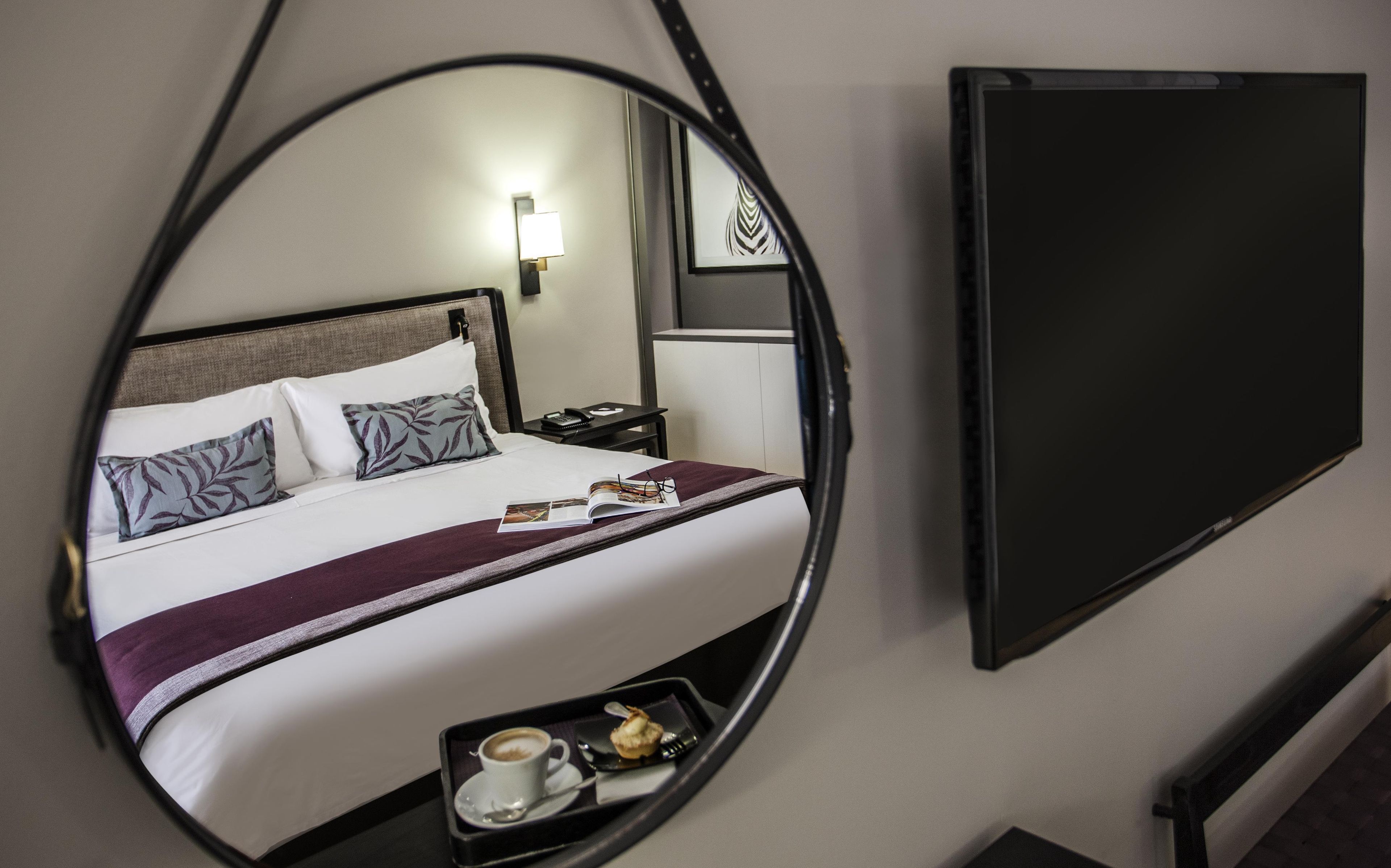 A hotel room with a bed, bedside table, lamp, and a flat-screen TV.