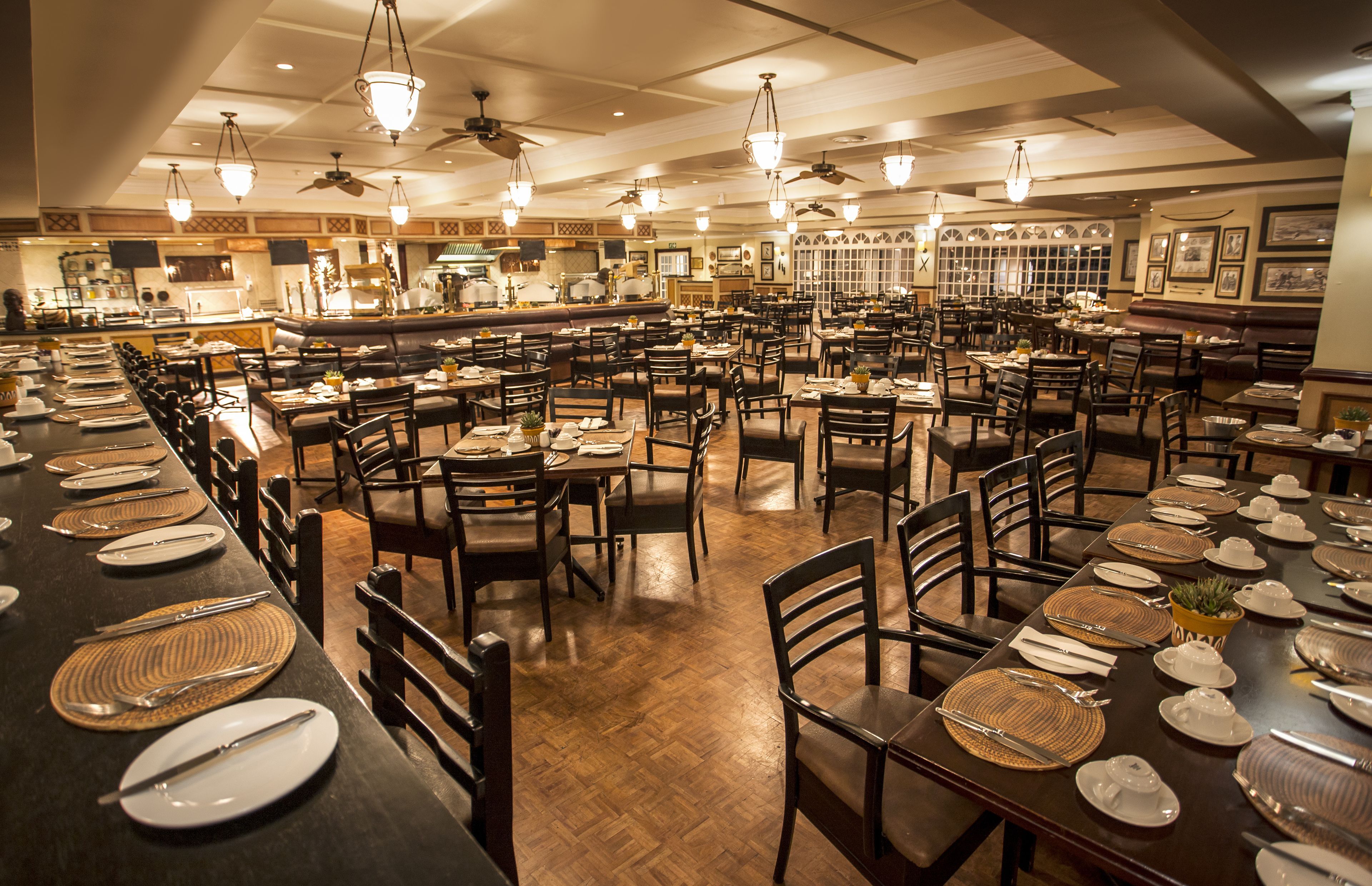 Un restaurante espacioso con varias mesas y sillas, una zona de bar y ventiladores de techo.
