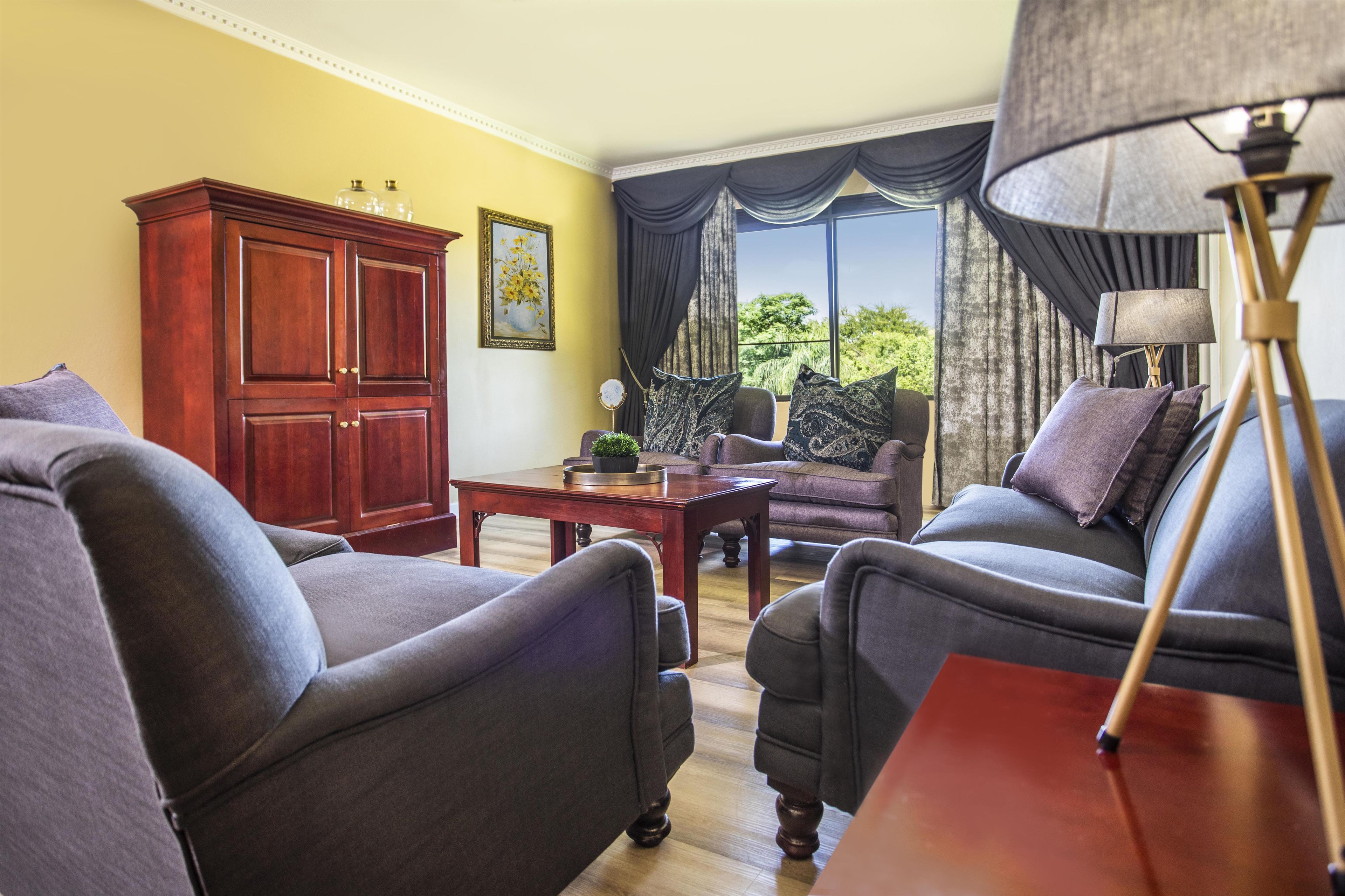 Sala de estar con dos sillones, un aparador de madera, una mesa y vistas al exterior con vegetación.