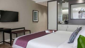 Quarto de hotel com cama, escrivaninha, cadeira, televisão e um espelho grande.