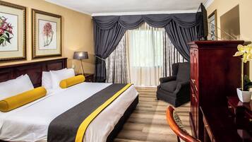 A hotel room with a large bed, a desk, a chair, and a window with curtains.