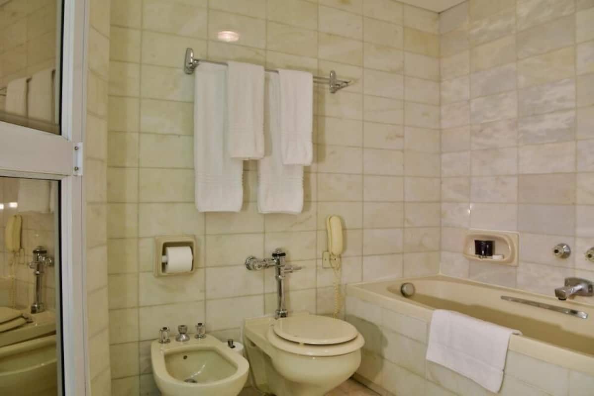 Une salle de bain équipée d’un bidet, de toilettes et d’une baignoire. Des serviettes sont accrochées au mur, et il y a un téléphone.