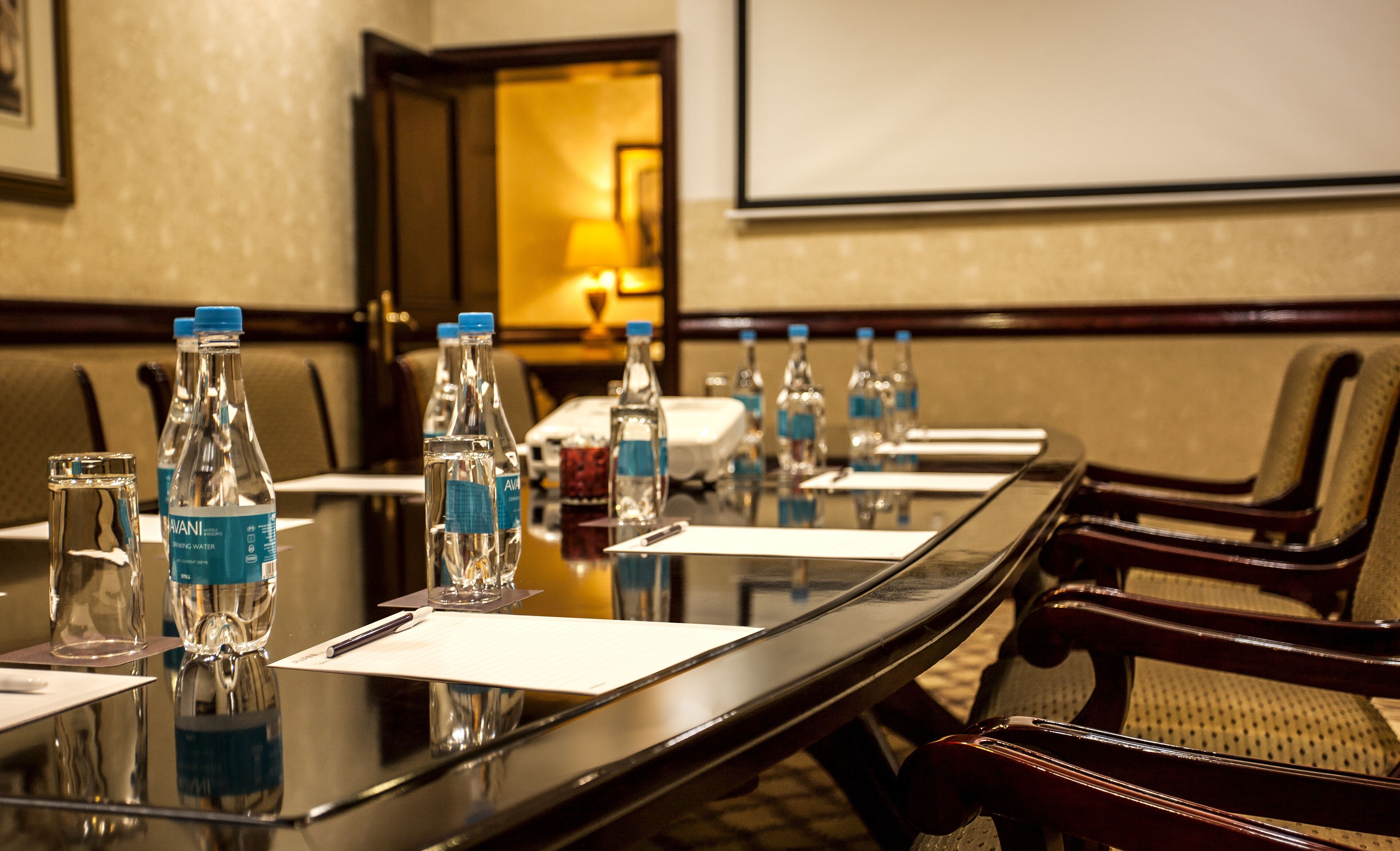 A conference room with a long table, chairs, water bottles, and a projector screen.