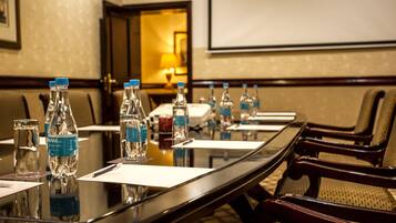 A conference room with a long table, chairs, water bottles, and a projector screen.
