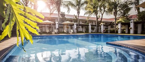 A swimming pool with a clear blue water surface, surrounded by palm trees and lounge chairs.