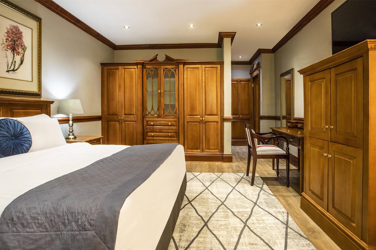 Une chambre d’hôtel avec un grand lit, une armoire en bois, un bureau et une chaise.
