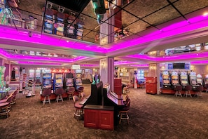 Interior de un casino con múltiples máquinas de juego, sillas y una zona de bar.