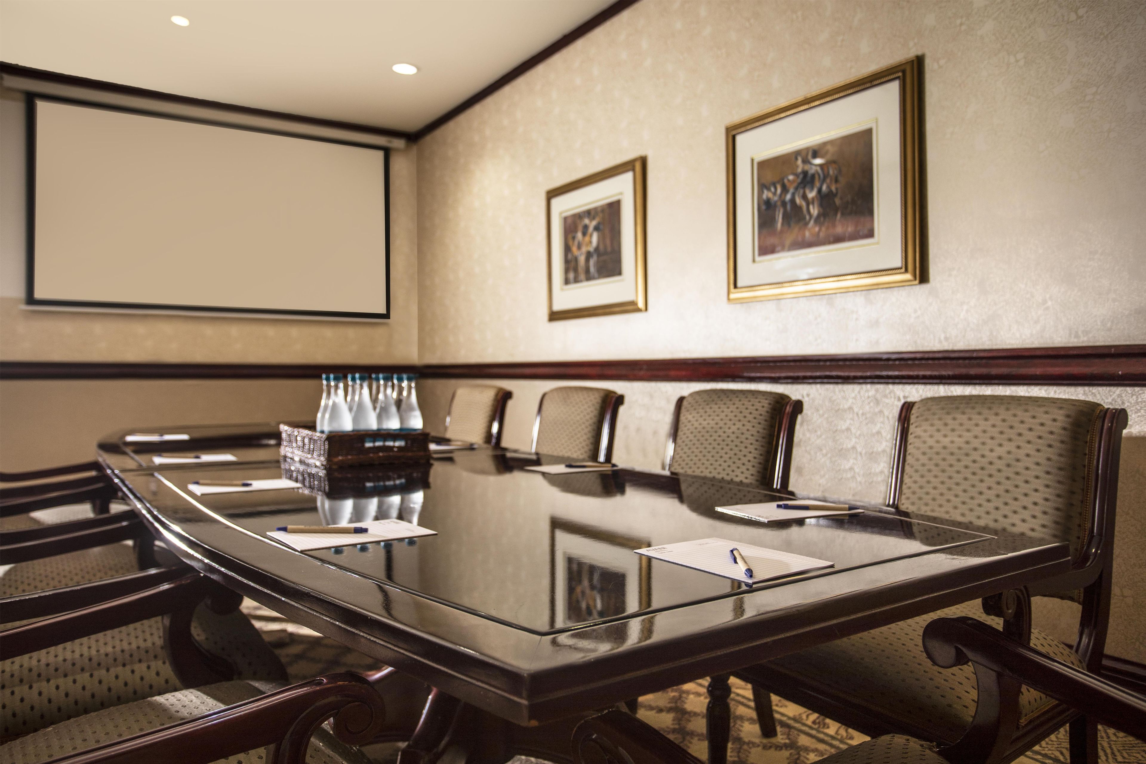 Un salón de conferencias con una mesa de vidrio, sillas, una pantalla de proyector y cuadros en la pared.
