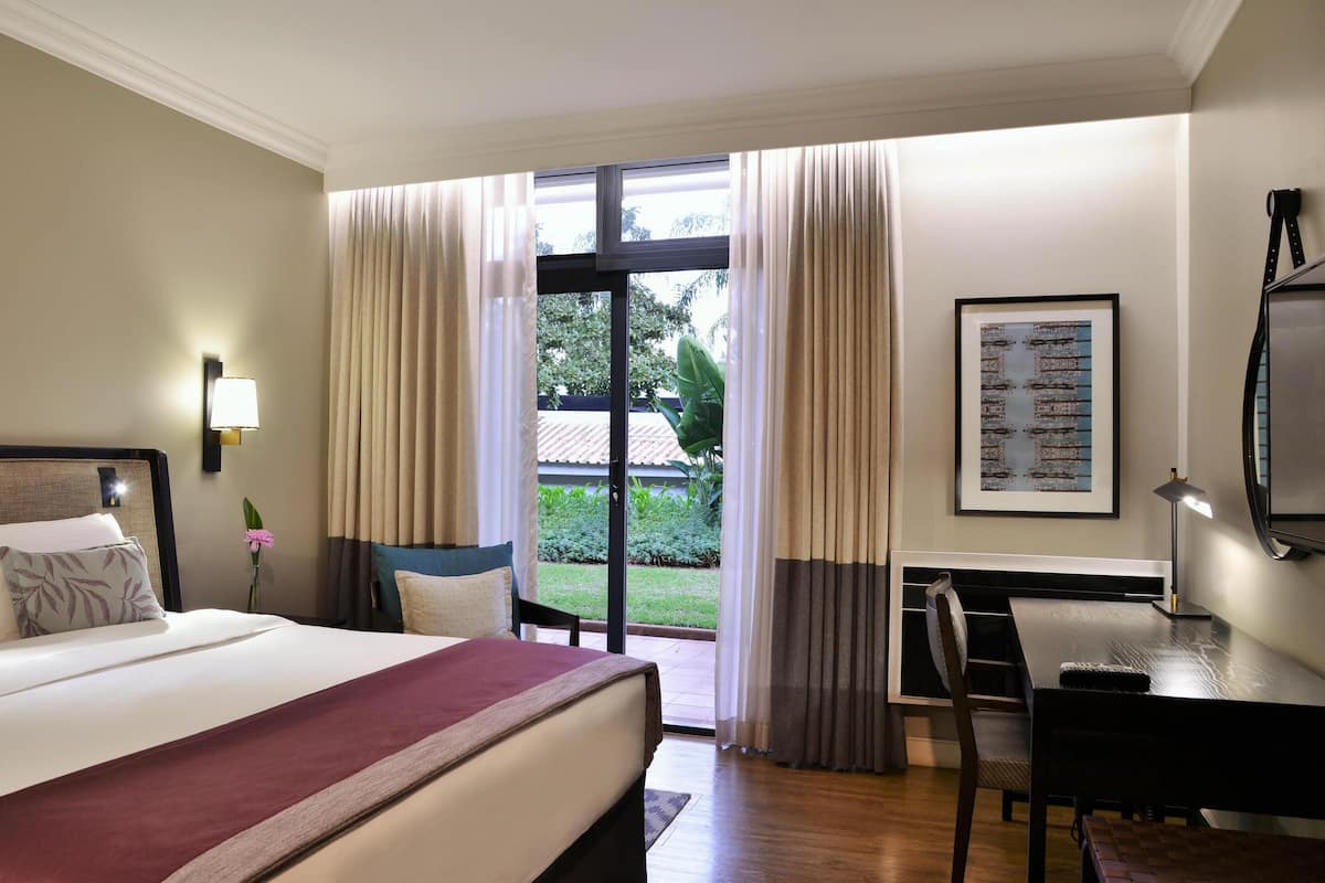 Une chambre d’hôtel avec un grand lit, un bureau, une chaise, une télévision et une fenêtre avec des rideaux.